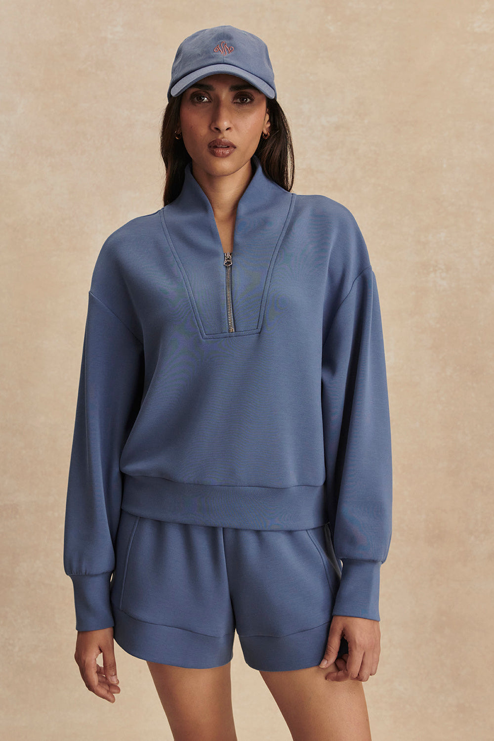 Woman wearing a blue tracksuit and cap on a beige background