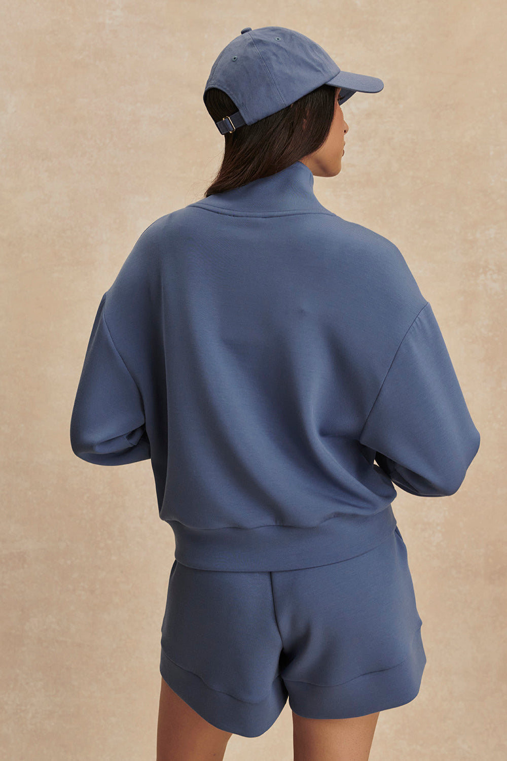 Person wearing a blue tracksuit and cap on a beige background