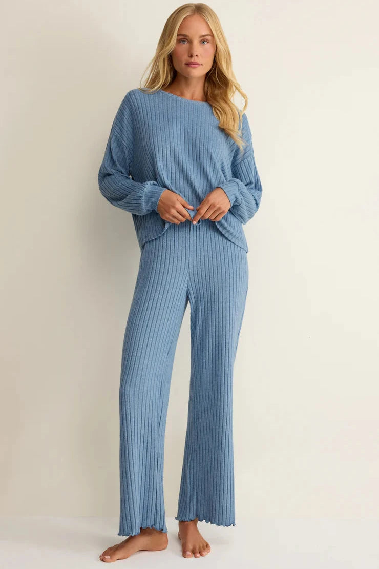 Woman wearing a blue ribbed sweater and pants on a beige background