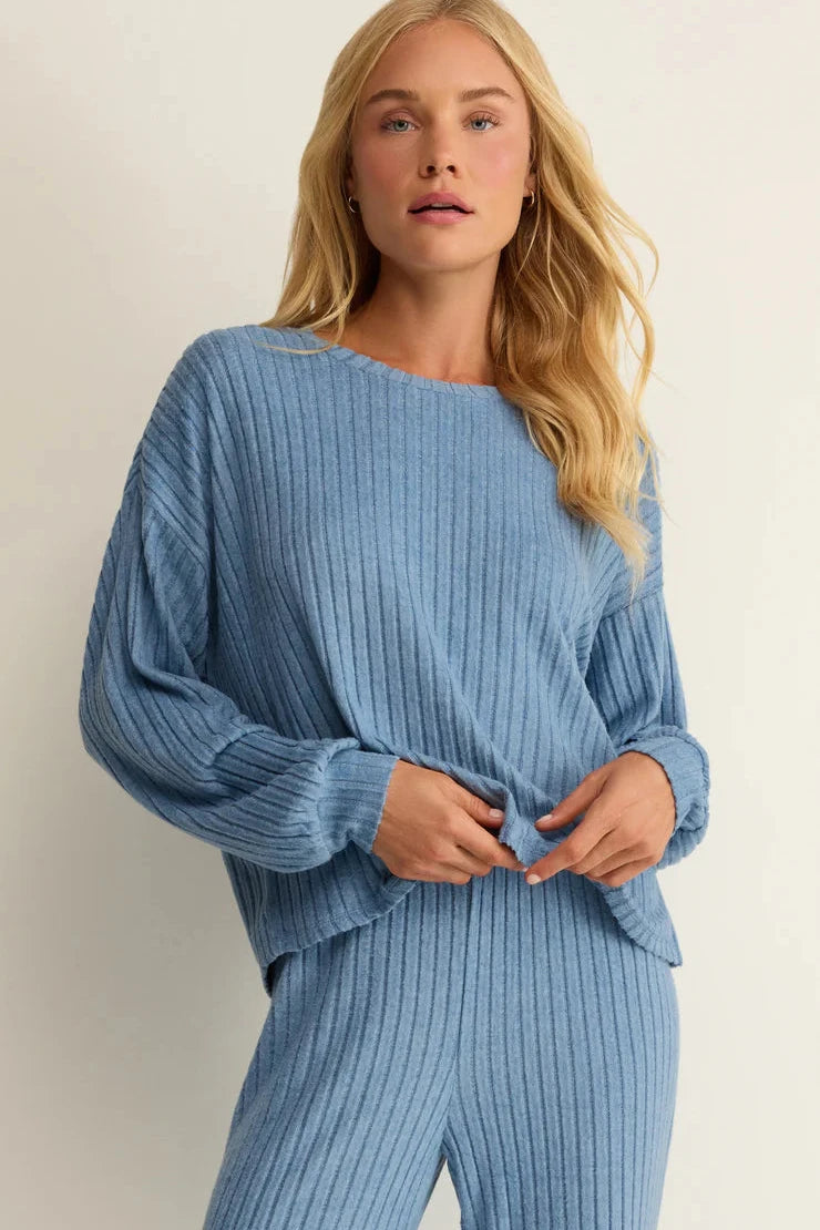 Woman wearing a blue ribbed sweater and pants against a plain background