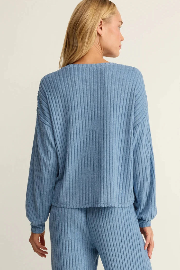 Woman wearing a blue ribbed sweater and pants on a beige background