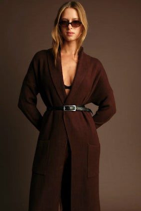 Woman wearing a brown coat and sunglasses against a plain background