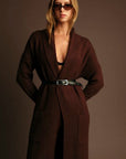 Woman wearing a brown coat and sunglasses against a plain background