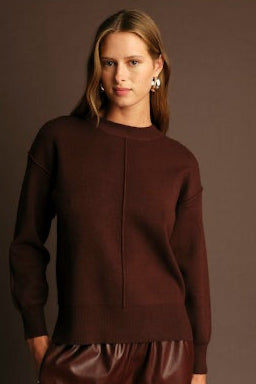 Woman wearing a brown sweater and pants against a dark background