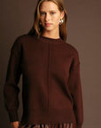 Woman wearing a brown sweater and pants against a dark background
