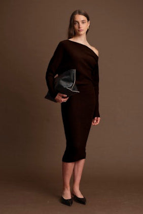 Woman wearing a black off-shoulder dress holding a clutch against a brown background