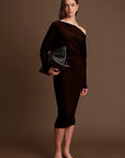 Woman wearing a black off-shoulder dress holding a clutch against a brown background