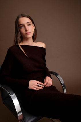 Woman in a brown off-shoulder top sitting on a modern chair against a brown background
