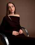 Woman in a brown off-shoulder top sitting on a modern chair against a brown background