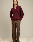Woman wearing a burgundy sweater and brown pants against a plain background