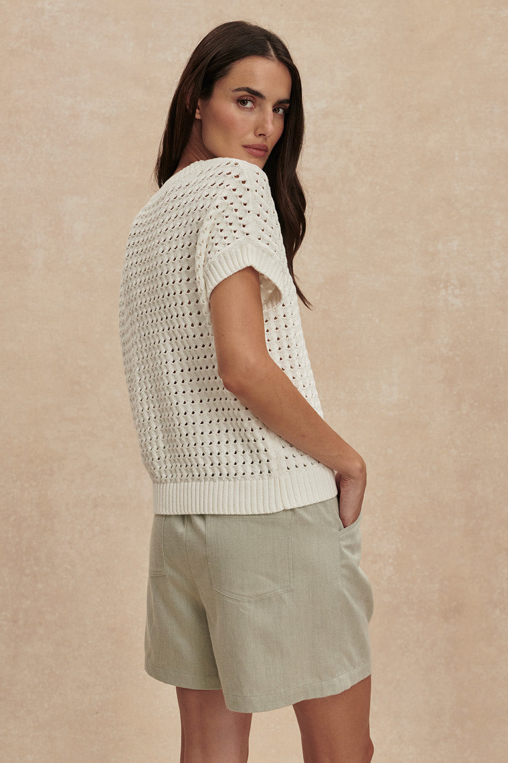 Woman wearing a white knit top and light green shorts against a beige background