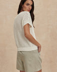 Woman wearing a white knit top and light green shorts against a beige background