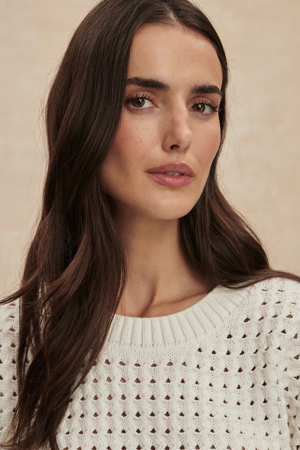 Woman wearing a white textured sweater against a beige background