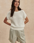 Woman wearing a white knitted sweater and light green shorts against a beige background
