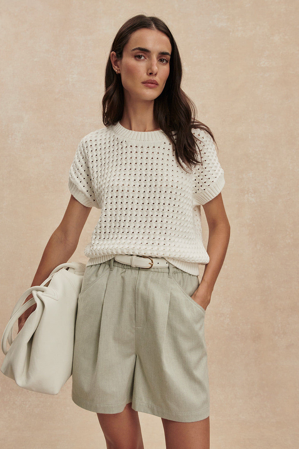 Woman wearing a white textured top and light green shorts against a beige background