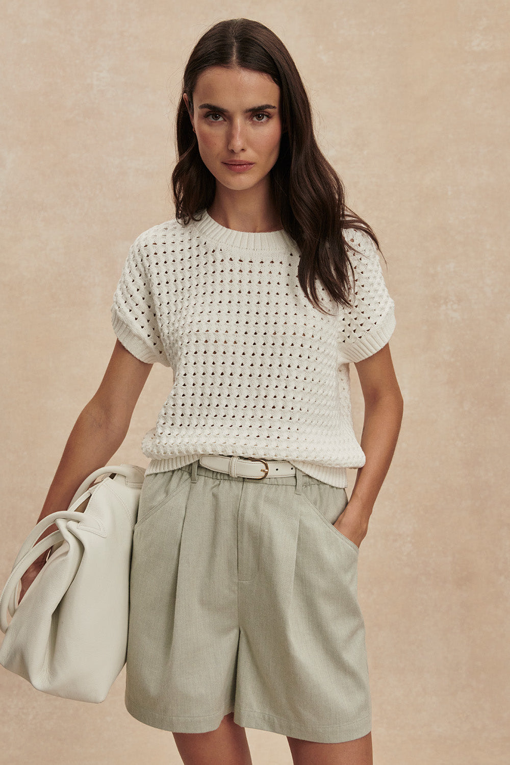 Woman wearing a white textured top and light green shorts against a beige background