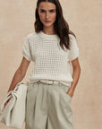 Woman wearing a white textured top and light green shorts against a beige background