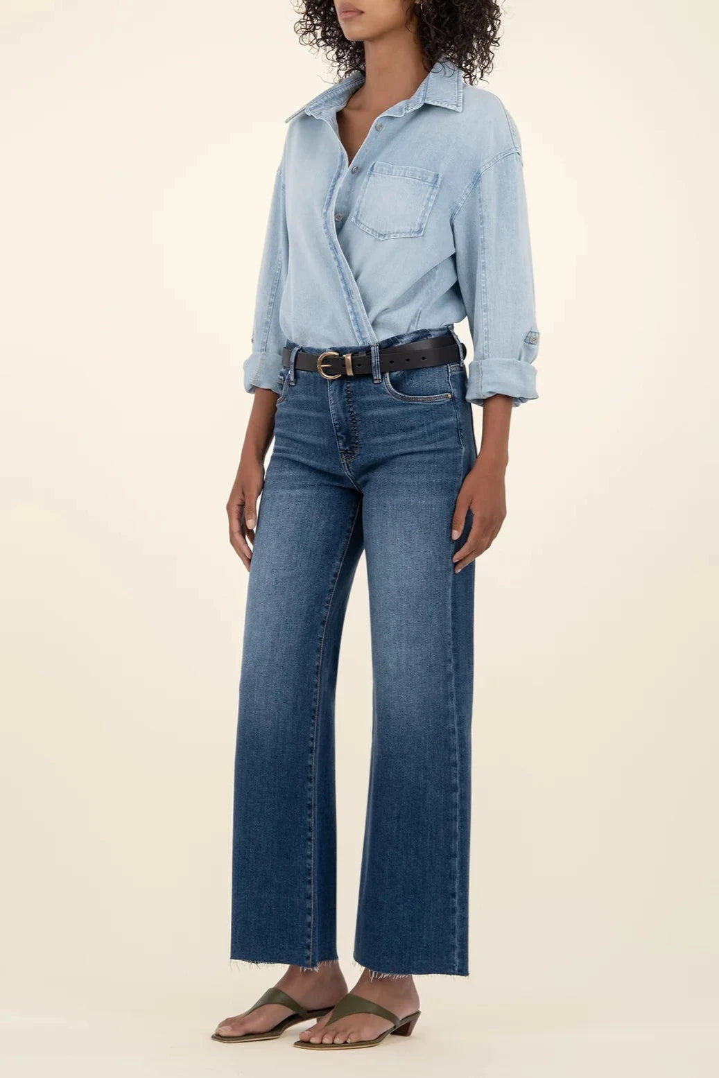 Person wearing a light blue denim shirt and dark blue jeans on a beige background