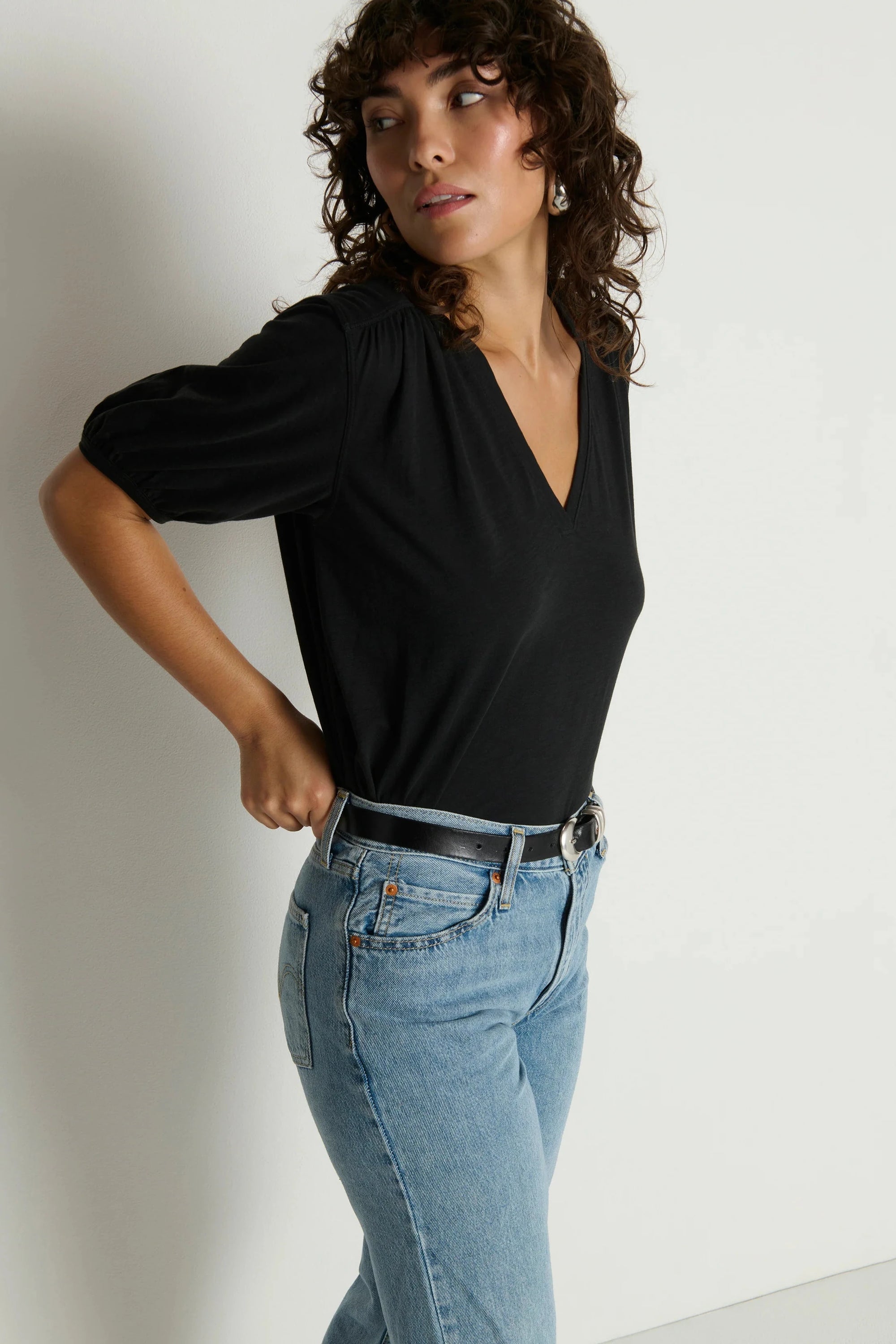 Woman wearing a black top and blue jeans against a plain background