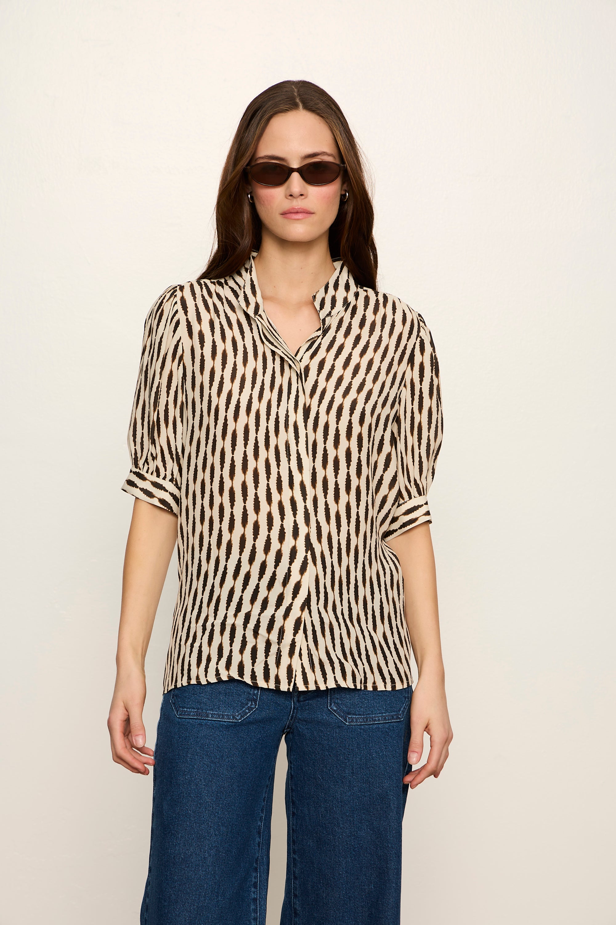 Woman wearing a patterned blouse and blue jeans against a plain background