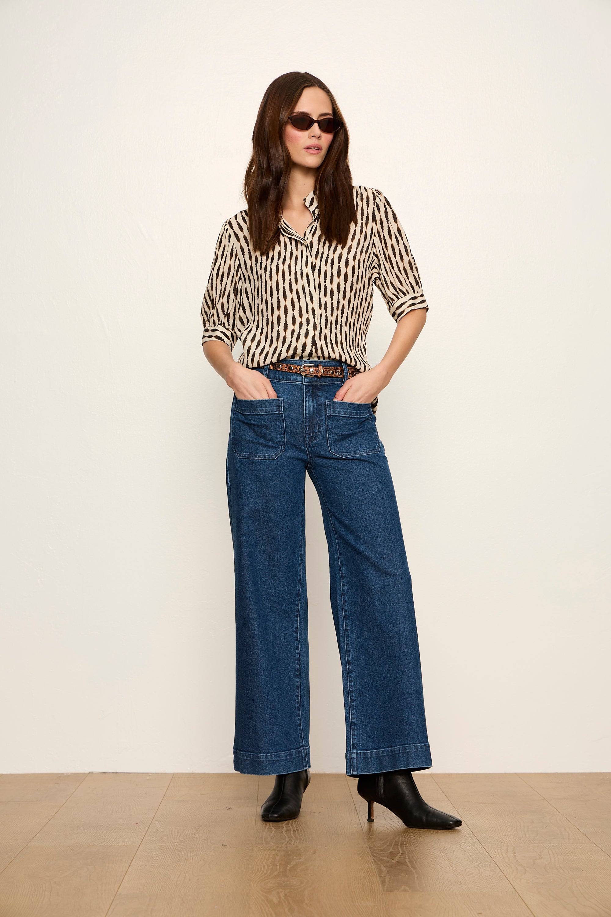 Woman wearing a patterned blouse and blue jeans against a white background