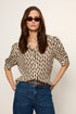 Woman wearing a zebra print top and blue jeans with sunglasses on a plain background