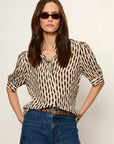 Woman wearing a zebra print top and blue jeans with sunglasses on a plain background