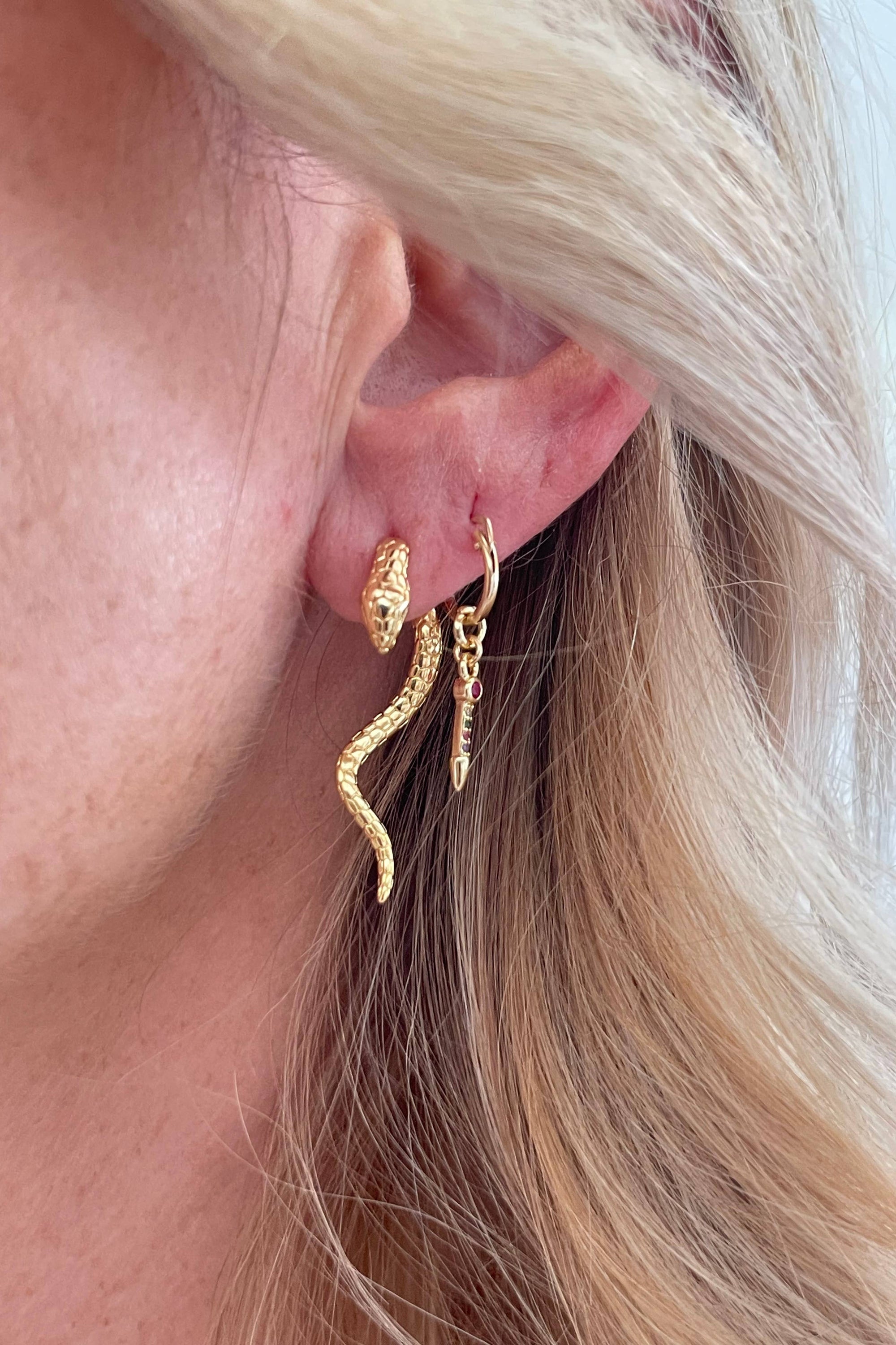 A close-up image of a person wearing gold-filled snake-shaped earrings.