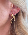 A close-up image of a person wearing gold-filled snake-shaped earrings.