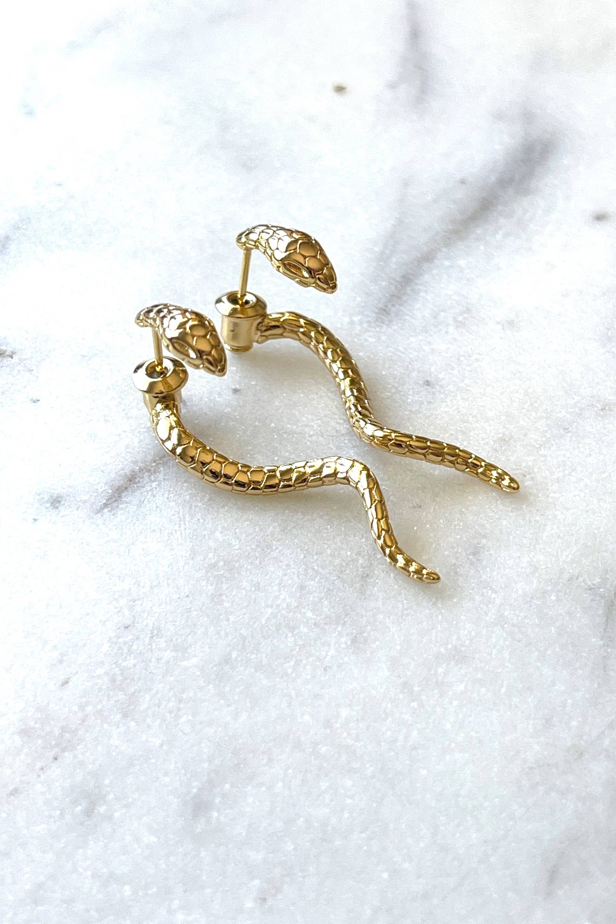 gold textured snake drop earrings on marble background