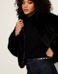Woman wearing a black fur coat and dark jeans against a plain background