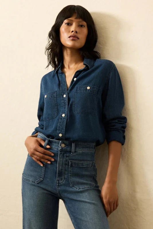 Woman wearing a blue denim shirt and jeans against a beige background