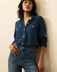 Woman wearing a blue denim shirt and jeans against a beige background