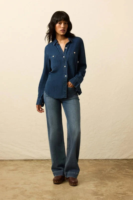 Woman wearing a blue denim shirt and jeans against a beige background