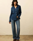 Woman wearing a blue denim shirt and jeans against a beige background