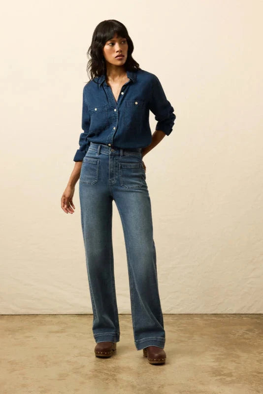 Woman wearing a blue denim shirt and jeans against a beige background