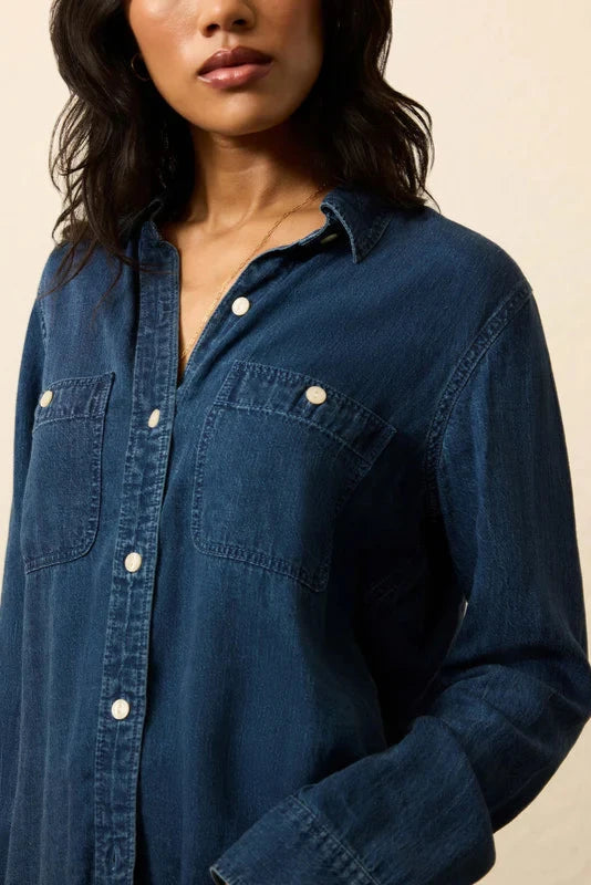 Person wearing a blue denim shirt against a beige background