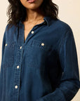 Person wearing a blue denim shirt against a beige background