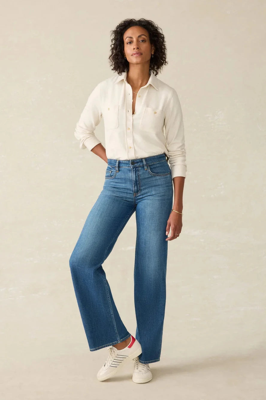 Woman wearing a white shirt and blue jeans against a beige background