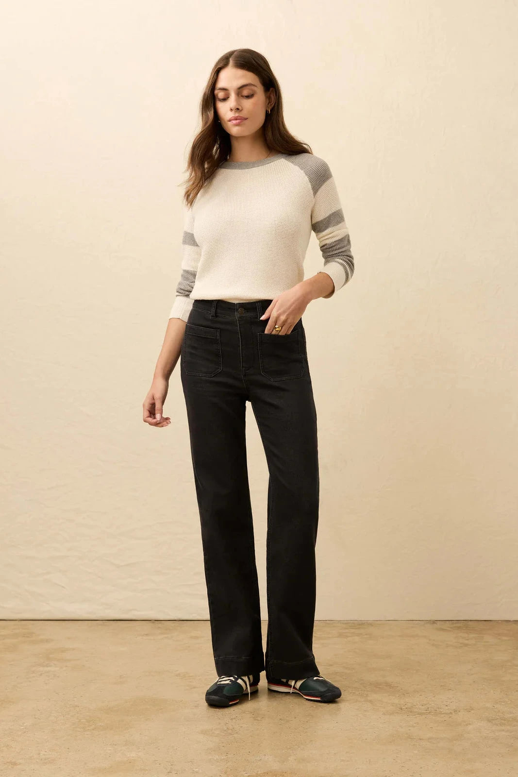 Woman wearing a striped sweater and black pants against a beige wall.