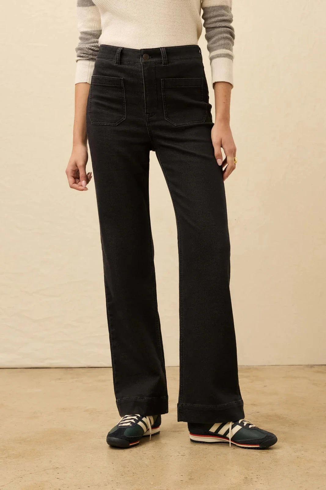 Person wearing black wide-leg pants and striped shoes on a beige background