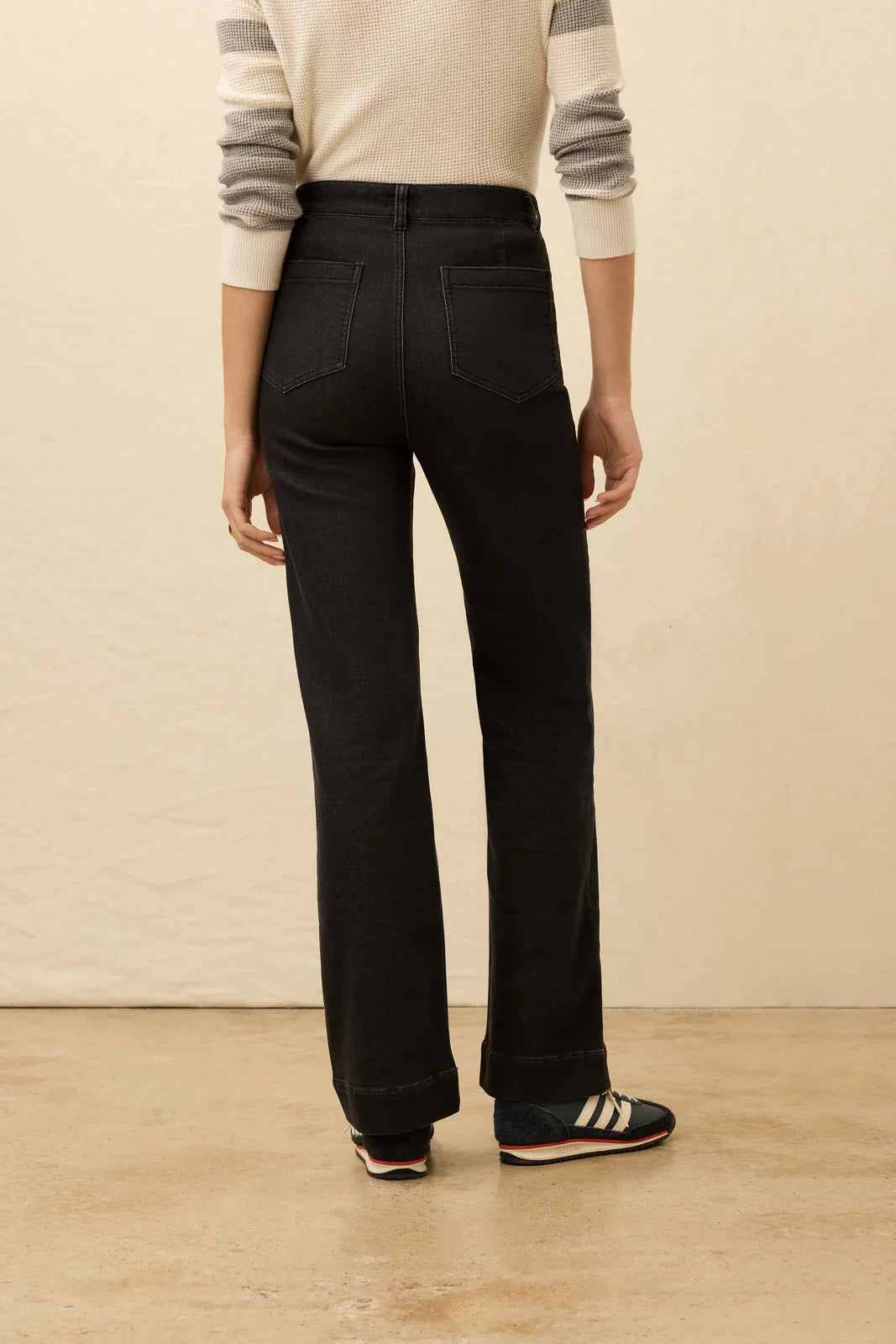 Person wearing black pants and a striped sweater on a beige background