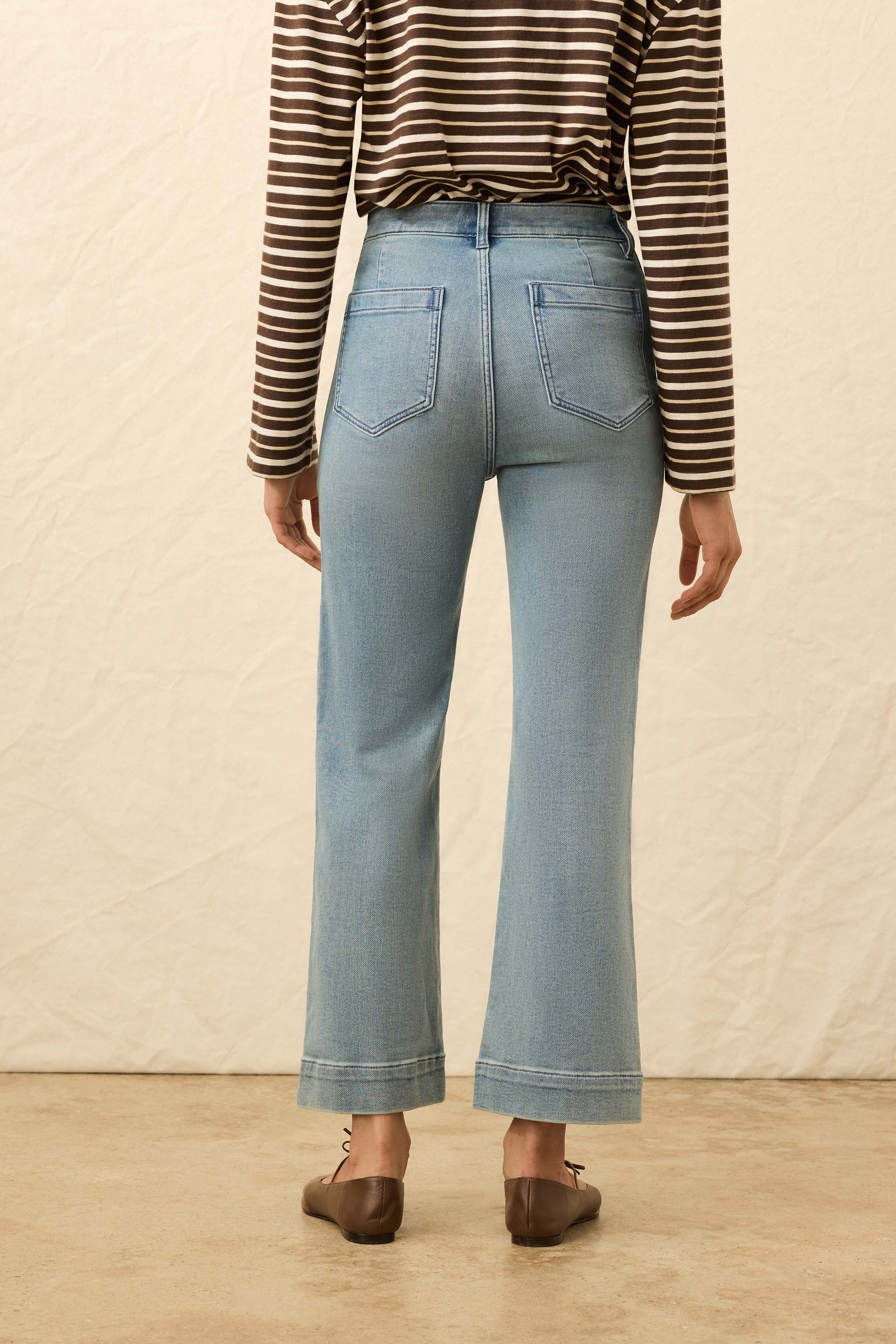 Person wearing light blue jeans and a striped shirt against a neutral background