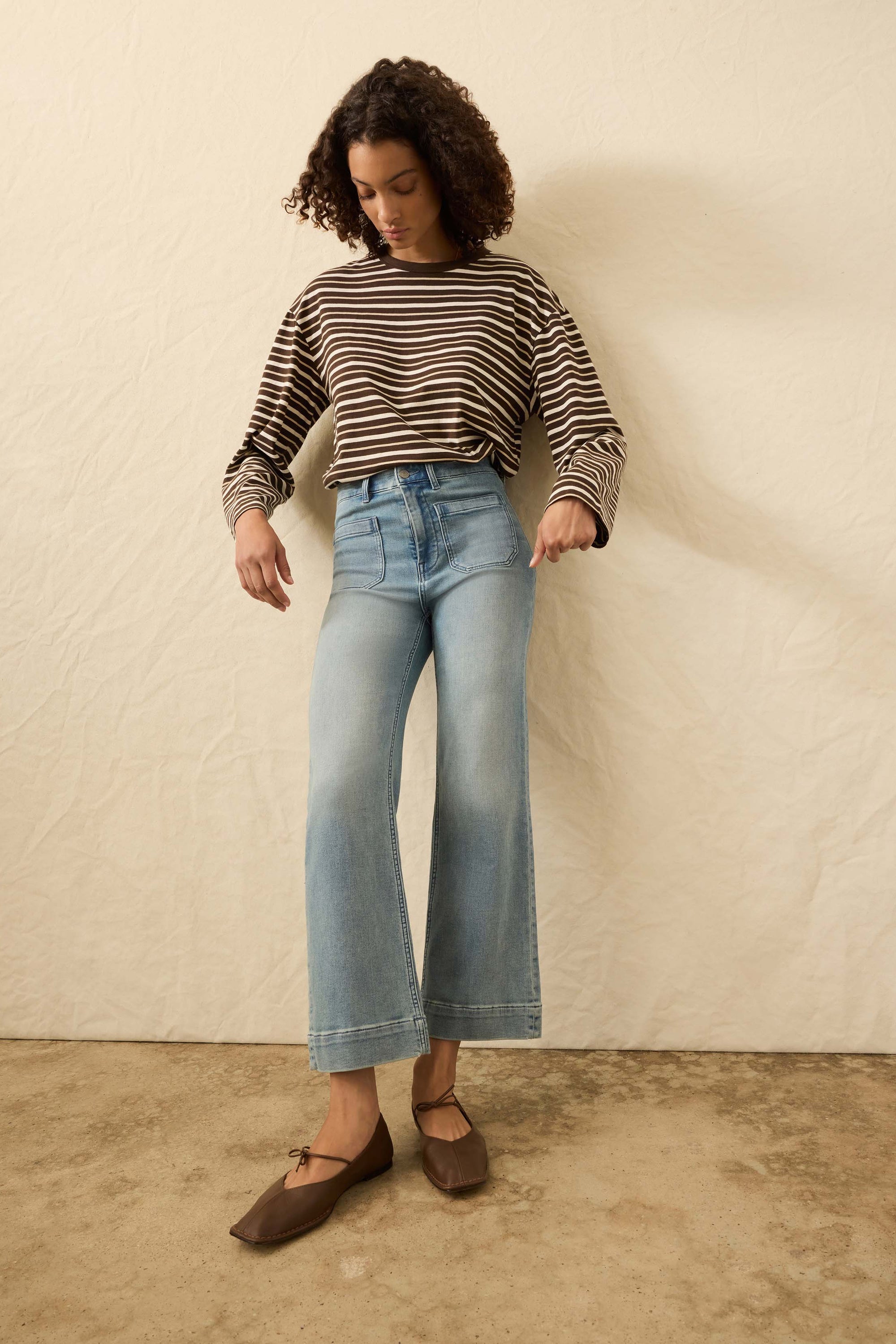 Woman wearing a striped sweater and blue jeans against a beige wall.