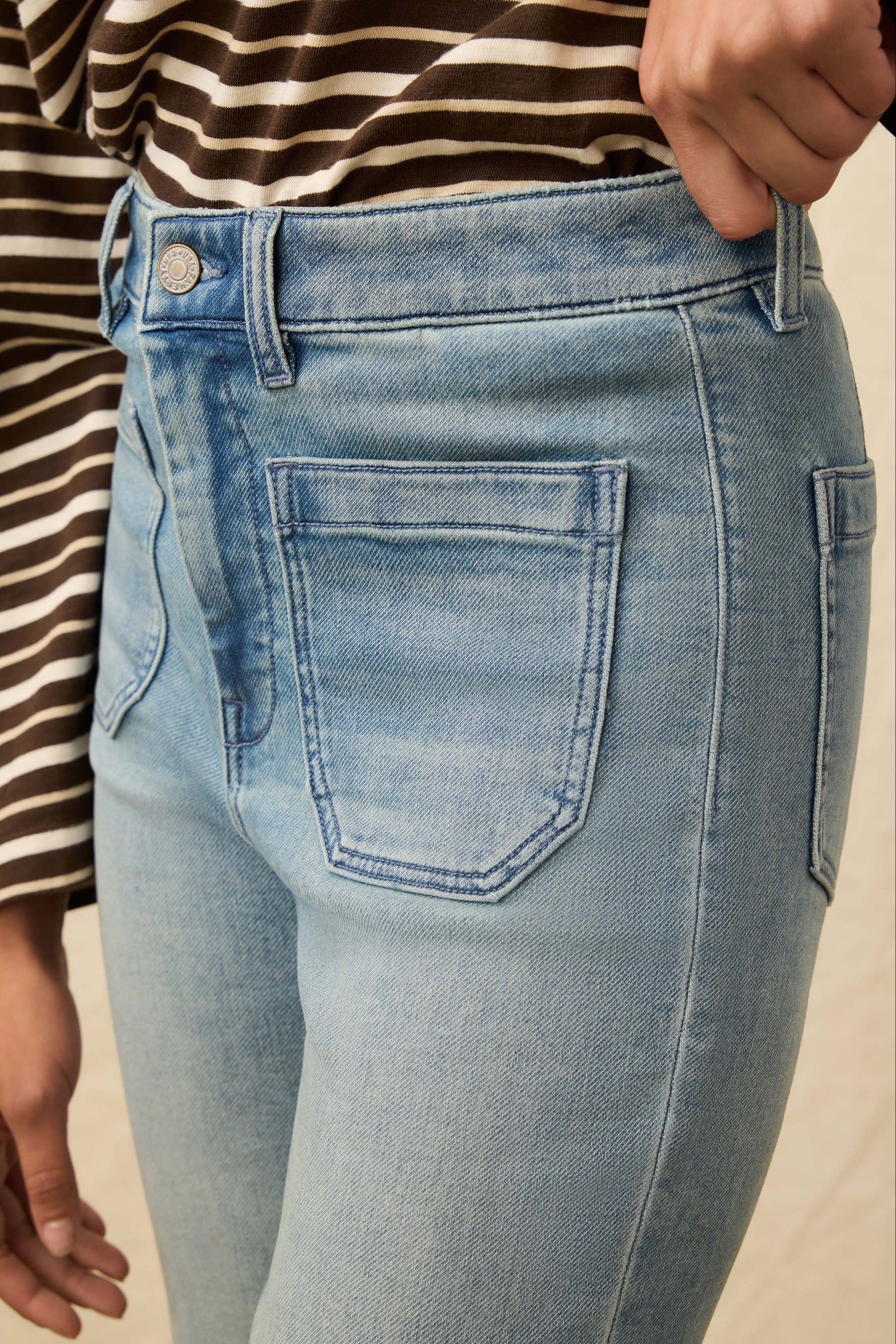 Light blue jeans worn by a person with a striped shirt on a beige background