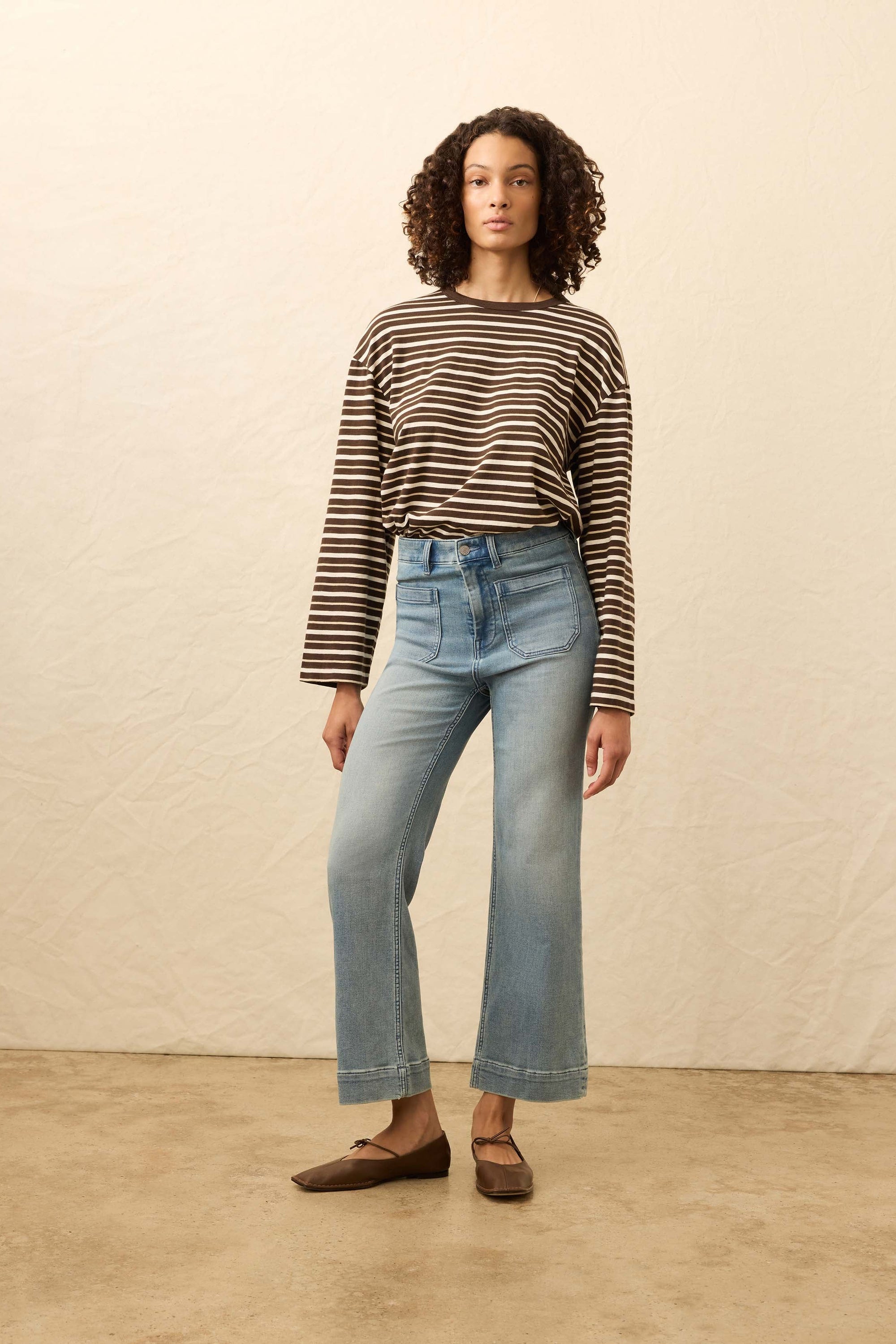 Woman wearing a striped sweater and light blue jeans against a beige background
