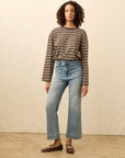 Woman wearing a striped sweater and light blue jeans against a beige background