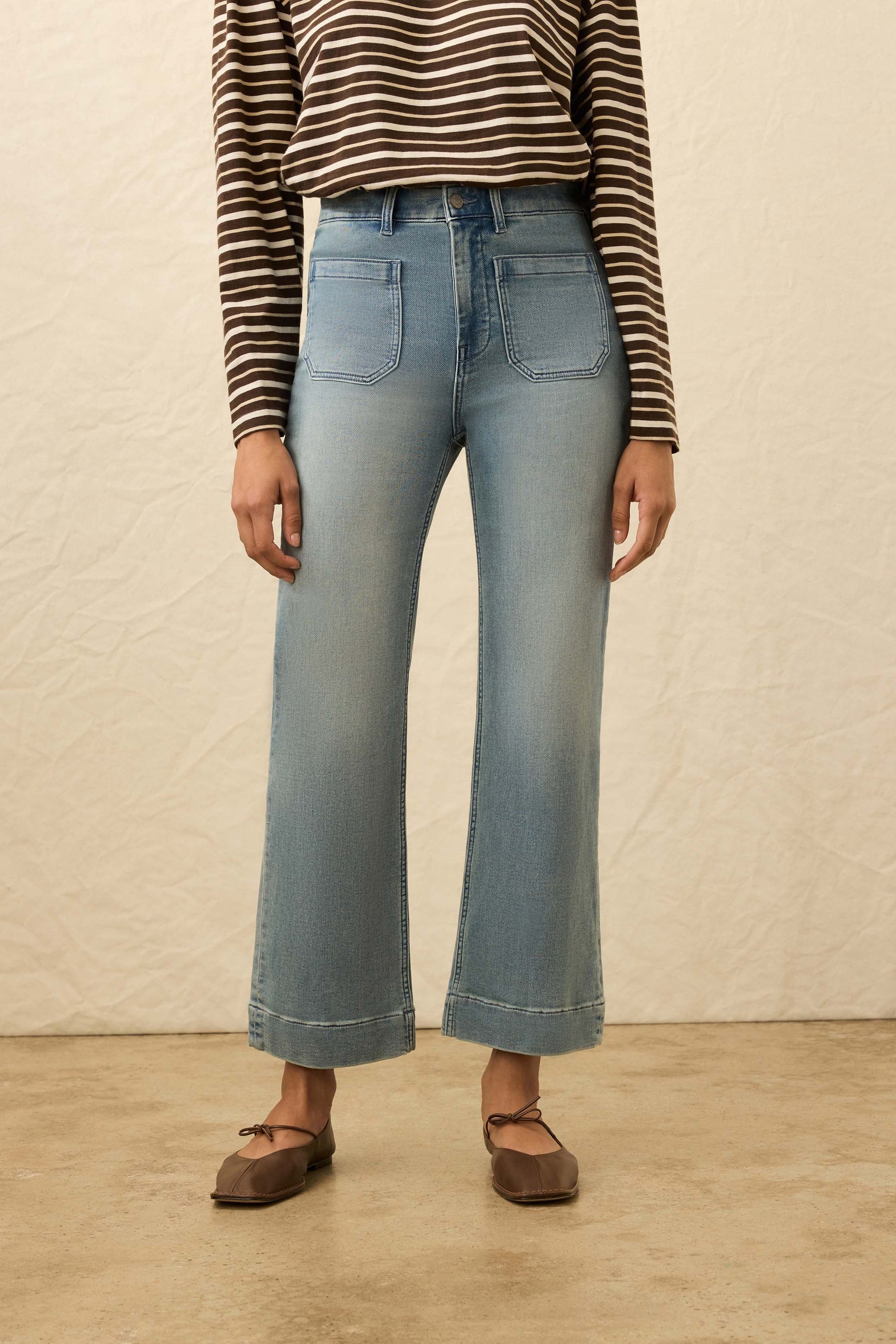 Person wearing a striped shirt and light blue jeans against a beige background