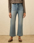 Person wearing a striped shirt and light blue jeans against a beige background