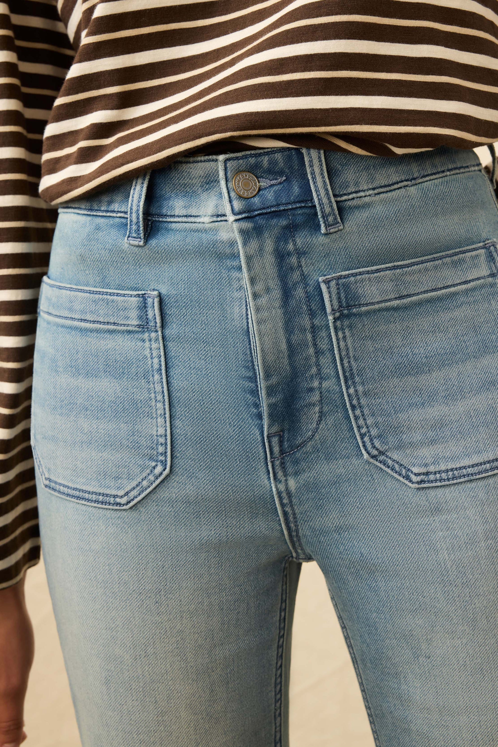 Close-up of blue jeans with a striped shirt worn underneath.